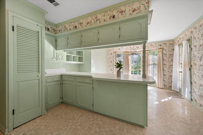 Kitchen featuring green cabinets, wallpapered walls, a peninsula, light countertops, and crown molding | Image 11