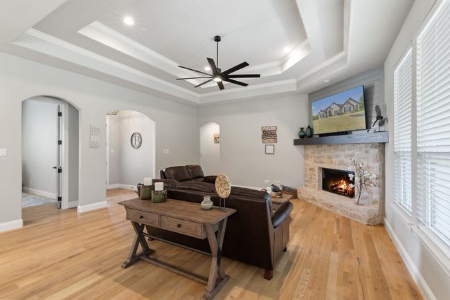 Living area with arched walkways, light wood-type flooring, a ceiling fan, a stone fireplace, and a raised ceiling | Image 7