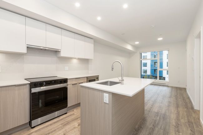 Kitchen with electric range oven, a sink, modern cabinets, under cabinet range hood, and recessed lighting | Image 9