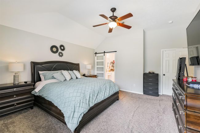 The primary bedroom features vaulted ceiling, recent ceiling fan and barn door closure to the primary bathroom. | Image 11
