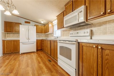 Kitchen featuring hanging light fixtures, lofted ceiling, a chandelier, white appliances, and light laminate wood-style flooring | Image 3