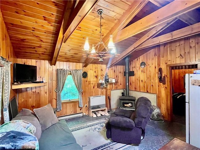 Featuring a wood stove, lofted ceiling with beams, wooden walls, and baseboard heating | Image 5