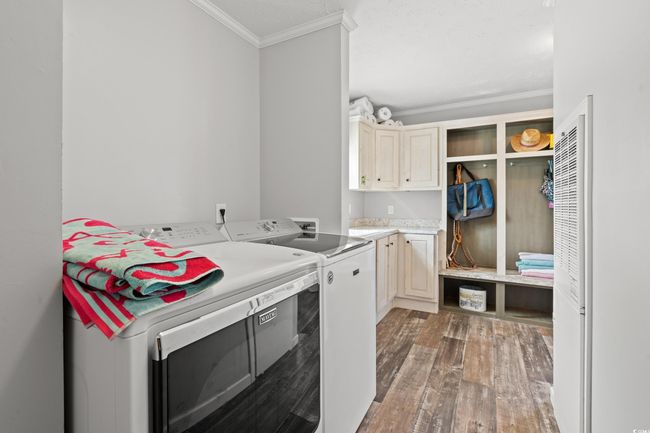 Laundry area featuring cabinet space, independent washer and dryer, crown molding, wood finished floors, and a heating unit | Image 19