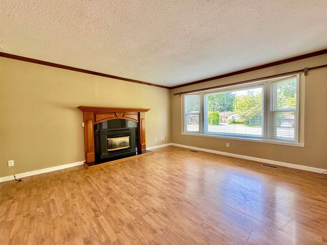 Unfurnished living room with light wood-type flooring, crown molding, a textured ceiling, and a glass covered fireplace | Image 4