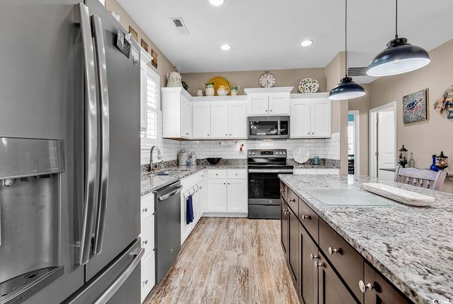 Kitchen with a kitchen island, a breakfast bar area, white cabinetry, stainless steel appliances, and visible vents | Image 13