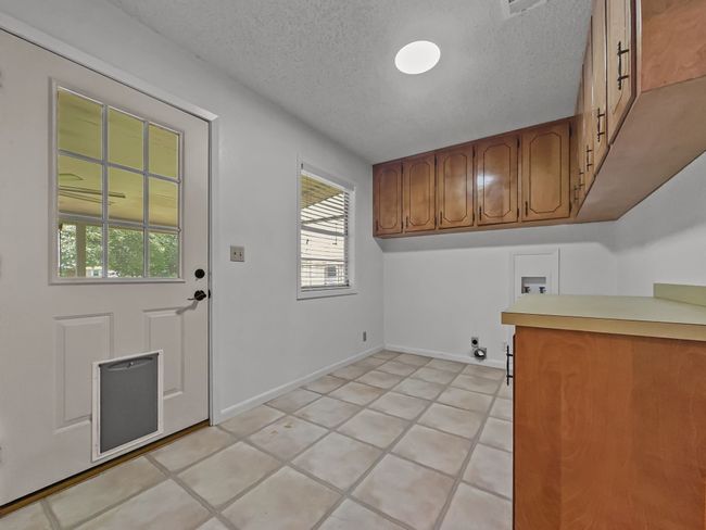 Washroom with cabinet space, a textured ceiling, hookup for a washing machine, electric dryer hookup, and light tile patterned floors | Image 13