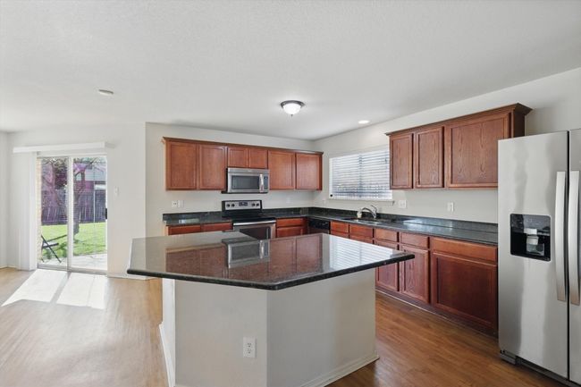 Kitchen featuring stainless steel appliances, wood finished floors, a kitchen island, a sink, and dark stone counters | Image 8