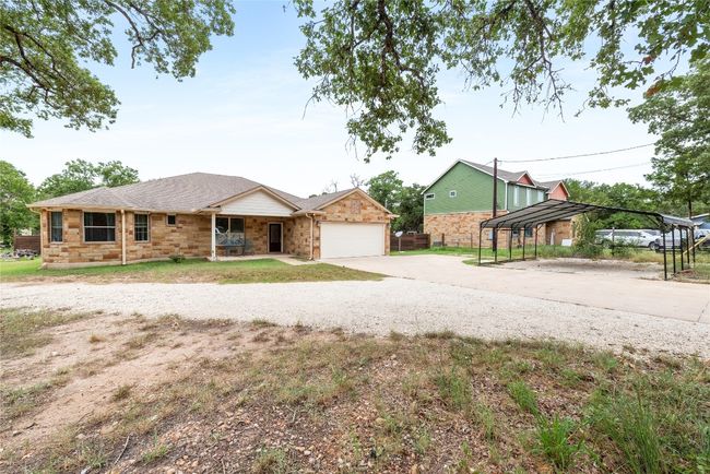 View of front of house with concrete driveway, an attached garage, stone siding, covered porch, and a shingled roof | Image 7