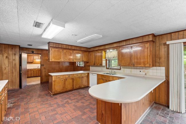 Kitchen with a sink, wood walls, a peninsula, light countertops, and brick floors | Image 12