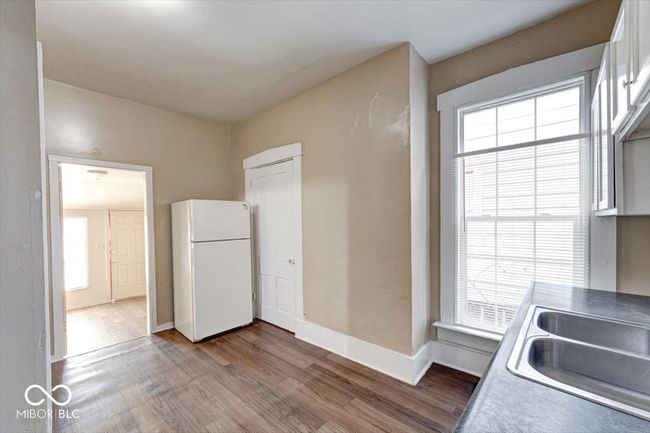 kitchen featuring baseboards, wood finished floors, freestanding refrigerator, a sink, and white cabinetry | Image 7
