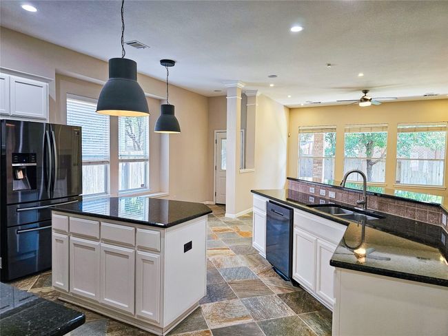 Kitchen with black fridge, dishwashing machine, a kitchen island, a sink, and stone tile floors | Image 12