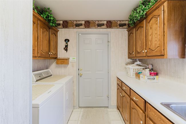 Laundry area featuring washing machine and dryer, cabinets, sink, and light tile patterned floors | Image 30