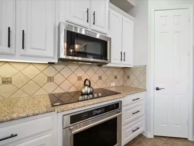 Kitchen featuring stainless steel appliances, white cabinetry, light stone counters, and backsplash | Image 6