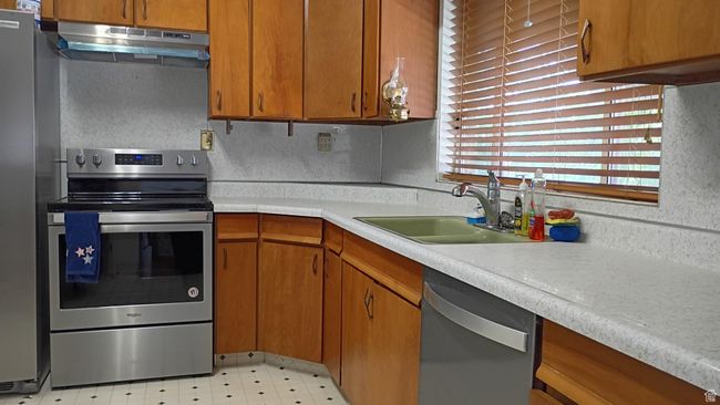 Kitchen featuring appliances with stainless steel finishes, light countertops, under cabinet range hood, and brown cabinetry | Image 18