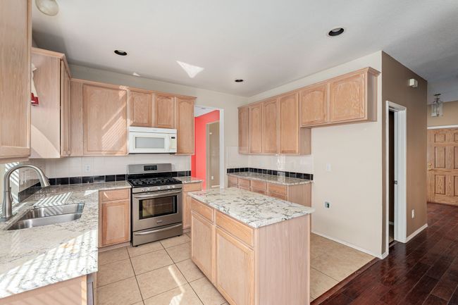 Kitchen featuring white microwave, stainless steel range with gas stovetop, light brown cabinetry, light stone counters, and recessed lighting | Image 9