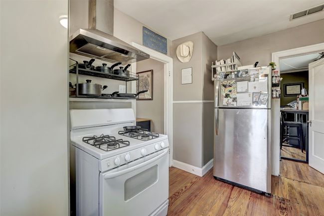 Kitchen with wood finished floors, white range with gas stovetop, wall chimney exhaust hood, visible vents, and freestanding refrigerator | Image 13