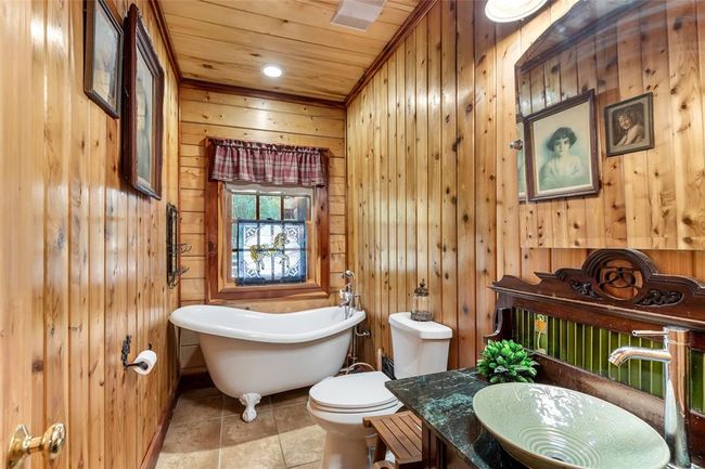 This cozy bathroom features rustic wood paneling, a vintage clawfoot bathtub, a modern vessel sink, and charming stained glass window accents. | Image 28
