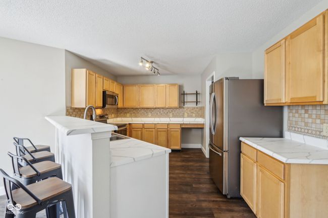 kitchen with appliances with stainless steel finishes, light brown cabinetry, a textured ceiling, a peninsula, and backsplash | Image 24