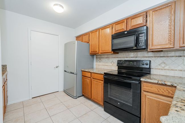 Kitchen featuring light stone countertops, light tile patterned floors, black appliances, and backsplash | Image 6