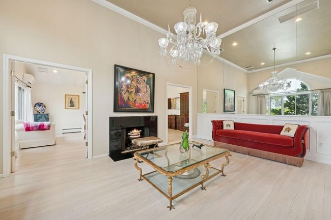 Living room featuring baseboard heating, a chandelier, an AC wall unit, a towering ceiling, and wood finished floors | Image 7