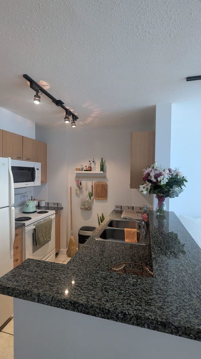 Kitchen featuring a textured ceiling, white appliances, a peninsula, and a sink | Image 10