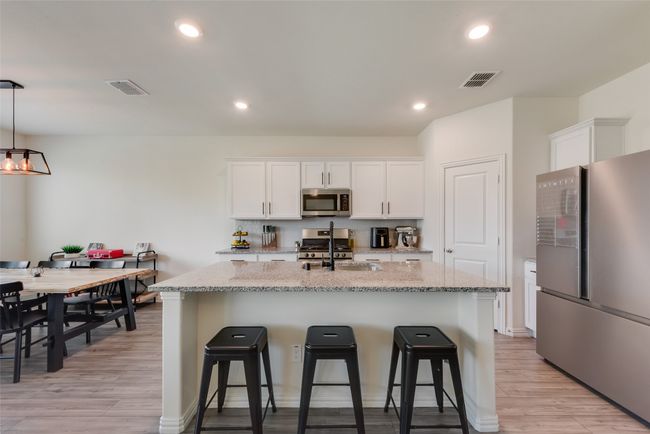 Kitchen featuring stainless steel appliances, a kitchen breakfast bar, an island with sink, light wood finished floors, and recessed lighting | Image 7