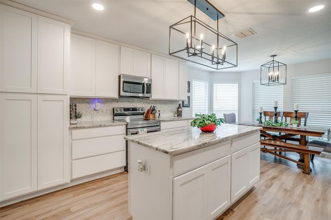 Kitchen with stainless steel appliances, a chandelier, light wood finished floors, tasteful backsplash, and a center island | Image 6