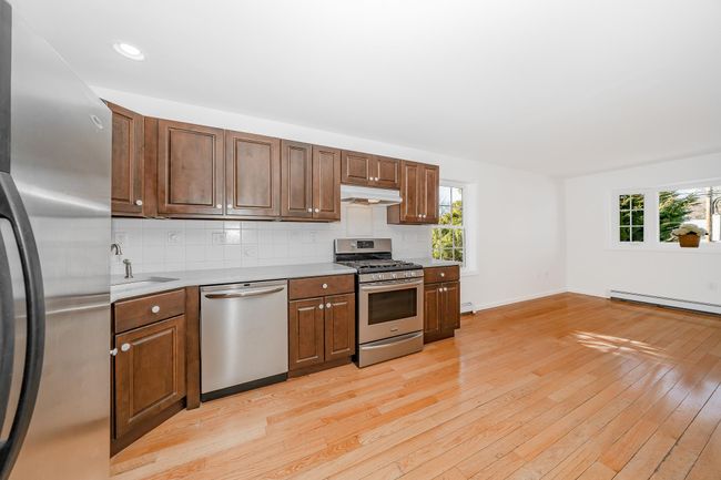 Kitchen featuring light wood-style flooring, appliances with stainless steel finishes, under cabinet range hood, a sink, and backsplash | Image 8