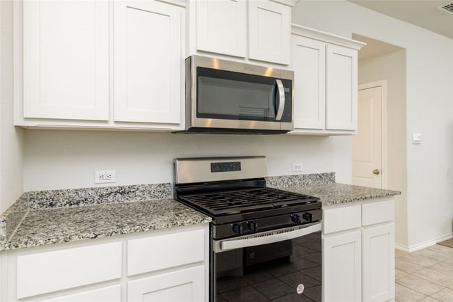 Kitchen featuring appliances with stainless steel finishes, white cabinets, light stone countertops, and light tile patterned floors | Image 12