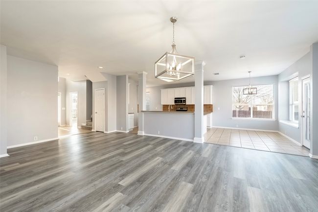 Unfurnished living room with a notable chandelier, light wood-style flooring, baseboards, and decorative columns | Image 20