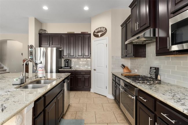 Kitchen with light stone counters, a sink, under cabinet range hood, stainless steel appliances, and arched walkways | Image 9