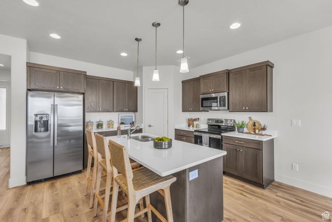 Kitchen with a kitchen breakfast bar, an island with sink, decorative light fixtures, light hardwood / wood-style floors, and stainless steel appliances | Image 11