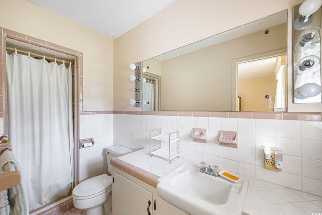 Full bath featuring tile walls, vanity, toilet, wainscoting, and shower / bathtub combination with curtain | Image 22
