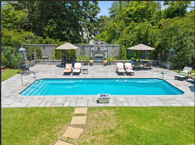 Outdoor pool with a fenced backyard, a patio area, an outdoor stone fireplace, and view of wooded area | Image 7
