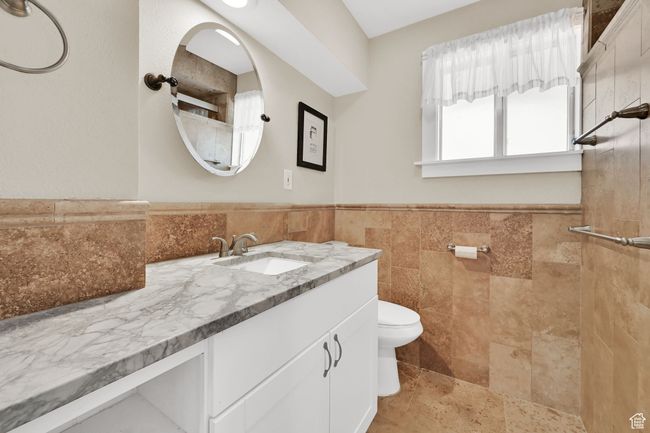 Full bathroom featuring a tile shower, toilet, vanity, tile walls, and wainscoting | Image 15