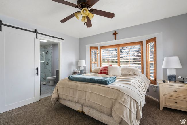 Carpeted bedroom featuring a barn door, connected bathroom, baseboards, and ceiling fan | Image 17