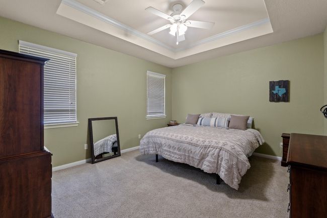 Carpeted bedroom featuring ornamental molding, a tray ceiling, baseboards, and a ceiling fan | Image 21