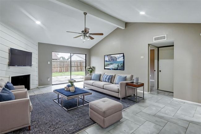 Step into the bright and airy living room, a perfect blend of comfort and style. High ceilings and sleek tiled floors create a spacious atmosphere, while the shiplap accent wall with a cozy fireplace adds a touch of rustic charm. The sliding glass doors provide seamless access to the backyard, inviting in natural light and offering a lovely view of your private outdoor retreat. | Image 4