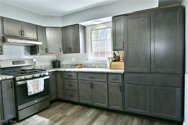 Kitchen featuring dark wood-style floors, stainless steel range with gas cooktop, under cabinet range hood, and backsplash | Image 16