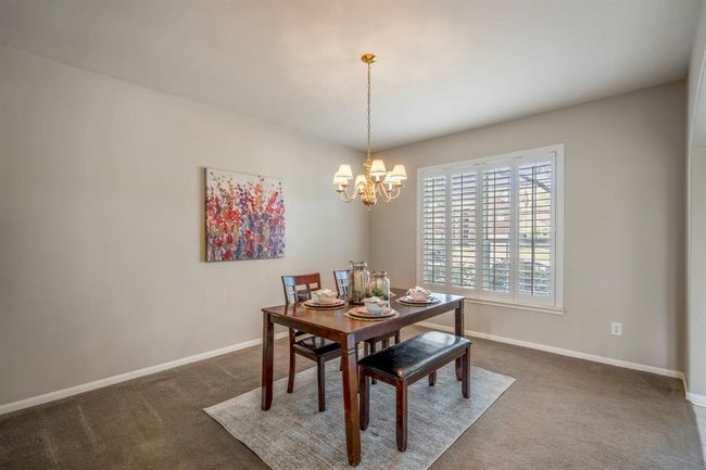 The spacious formal dining room offers an elegant setting for gatherings, featuring a large window with plantation shutters that provide natural light and a view of the front yard. | Image 5