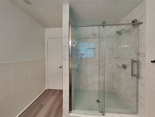 Bathroom with tile walls, wood finished floors, a textured ceiling, a marble finish shower, and wainscoting | Image 16