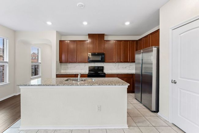 Kitchen with black appliances, decorative backsplash, light stone countertops, an island with sink, and recessed lighting | Image 6
