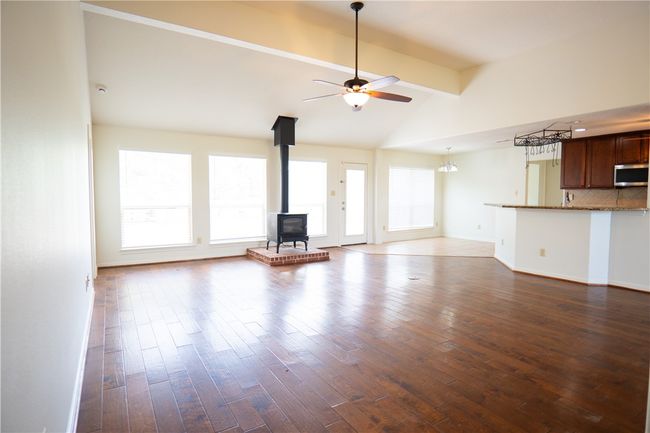 Unfurnished living room with a wood stove, a ceiling fan, dark wood-style floors, beam ceiling, and high vaulted ceiling | Image 17