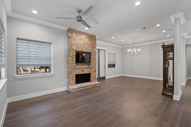 Unfurnished living room with ornamental molding, a stone fireplace, visible vents, and ceiling fan with notable chandelier | Image 4