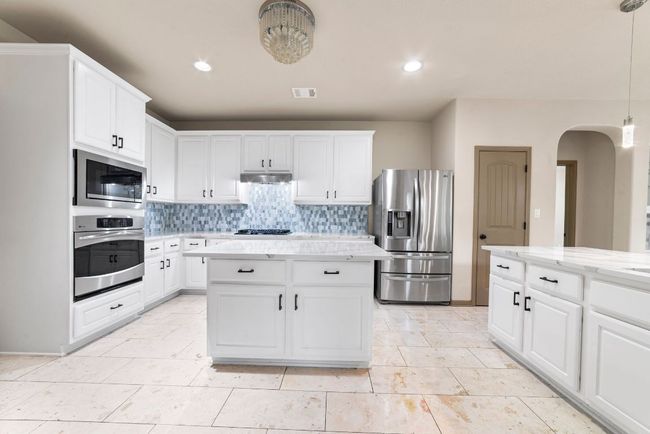 Kitchen featuring stainless steel appliances, arched walkways, tasteful backsplash, under cabinet range hood, and white cabinets | Image 17