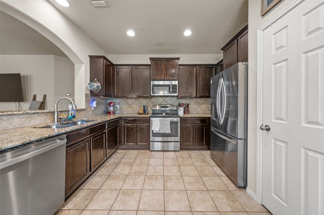 Kitchen with stainless steel appliances, light stone counters, dark brown cabinets, arched walkways, and decorative backsplash | Image 6