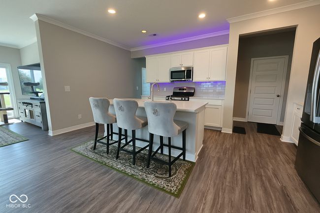 kitchen with appliances with stainless steel finishes, ornamental molding, dark wood-style flooring, a center island with sink, and light countertops | Image 4