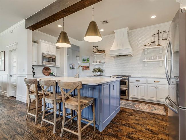 Kitchen featuring white cabinetry, light countertops, appliances with stainless steel finishes, custom exhaust hood, and open shelves | Image 6