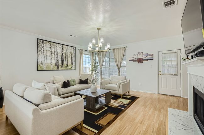 Living room with crown molding, a high end fireplace, light wood-style flooring, and a chandelier | Image 4