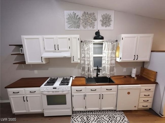 Kitchen with white appliances, white cabinets, dark wood finished floors, under cabinet range hood, and open shelves | Image 7